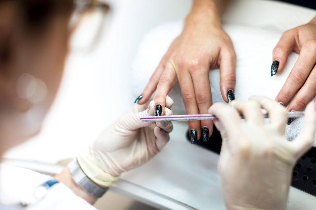 Manicurist using a file on a fingernail to remove excess cuticles and prepare it for painting